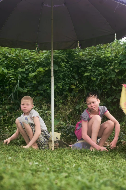 two little boys sitting under an umbrella in the grass