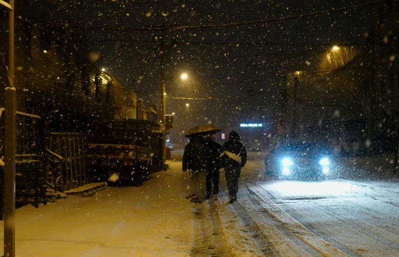 people walk in the snow on the sidewalk under a street lamp