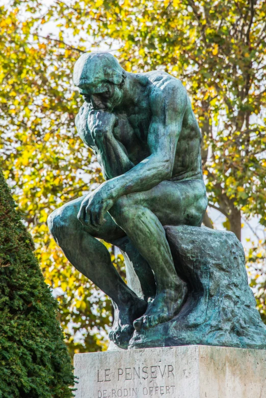 the thinker is seated in the shade of some trees