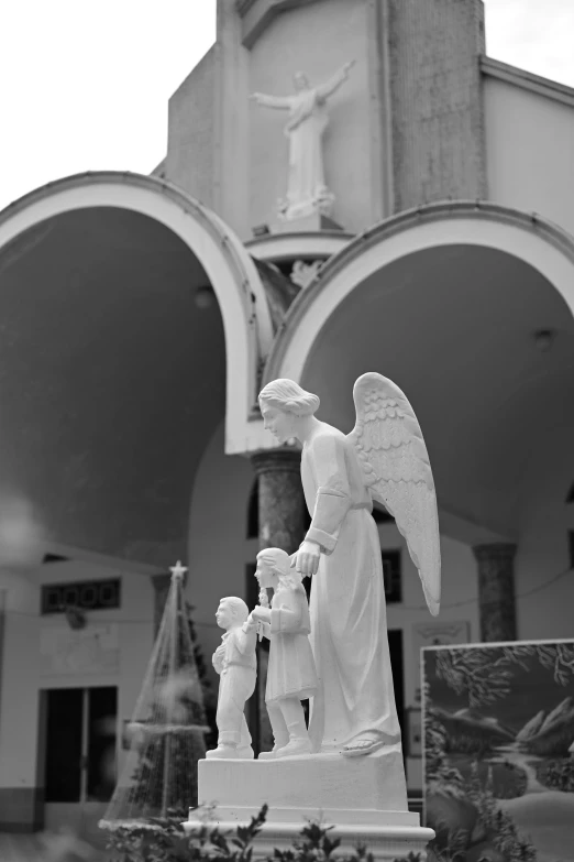 black and white po of statue in front of church with angel on pillar