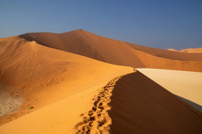 a sandy mountain with tracks in the sand and people on it