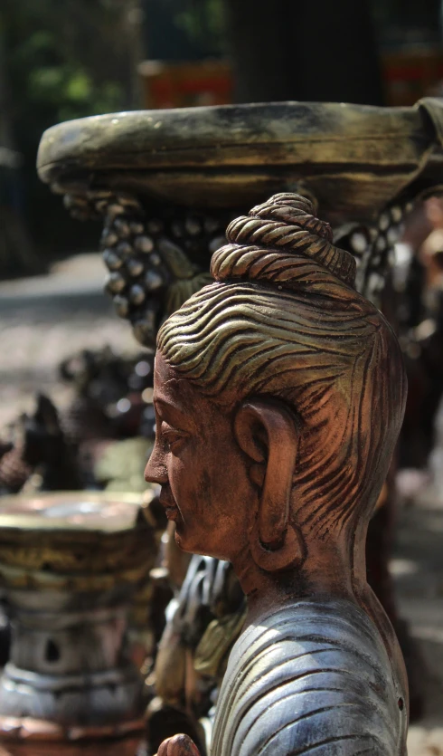 wooden carving of a woman sitting next to a metal bowl