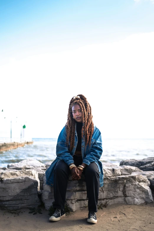 a girl with dreadlocks and a jacket sitting near the water