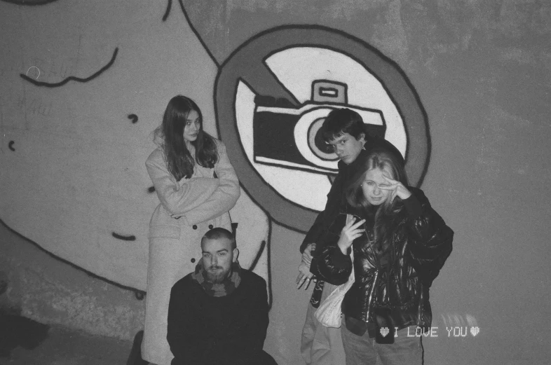 a group of young people stand in front of a graffiti covered wall