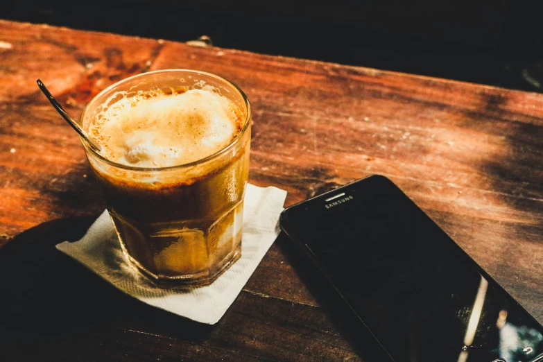 a glass of beer sits on the table beside an cell phone