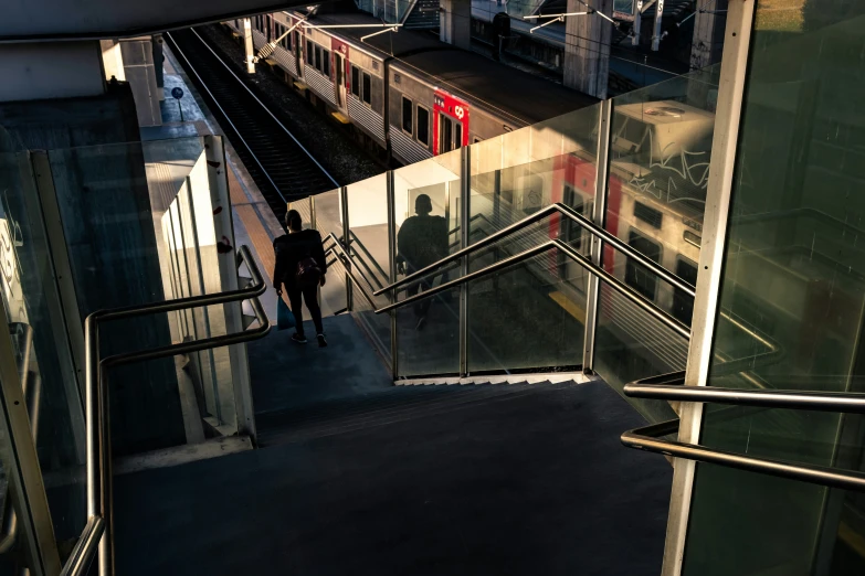 a person standing on an open set of stairs, looking down at a train