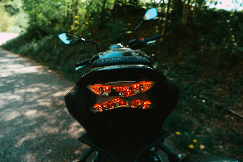 a motorcycle handle bar and tail lights reflected in the rear mirror