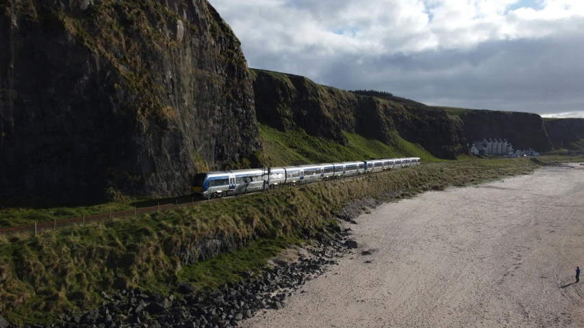 a train driving down tracks near a cliff and beach