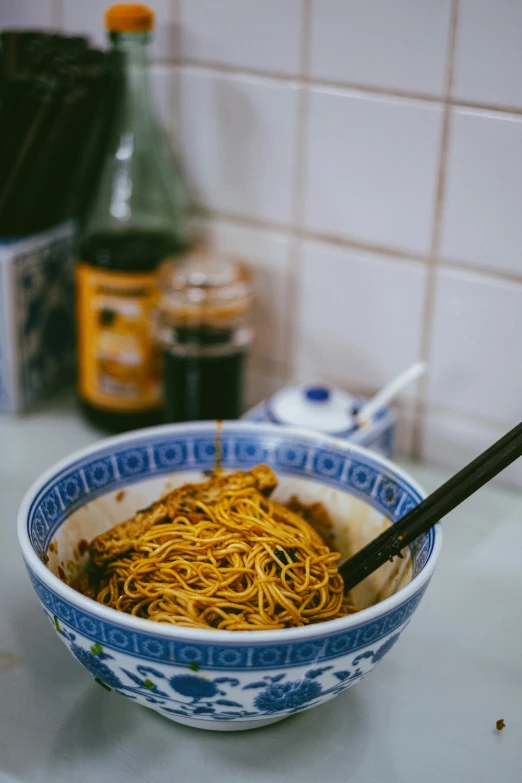 a bowl of noodles and chopsticks sit on a kitchen counter top