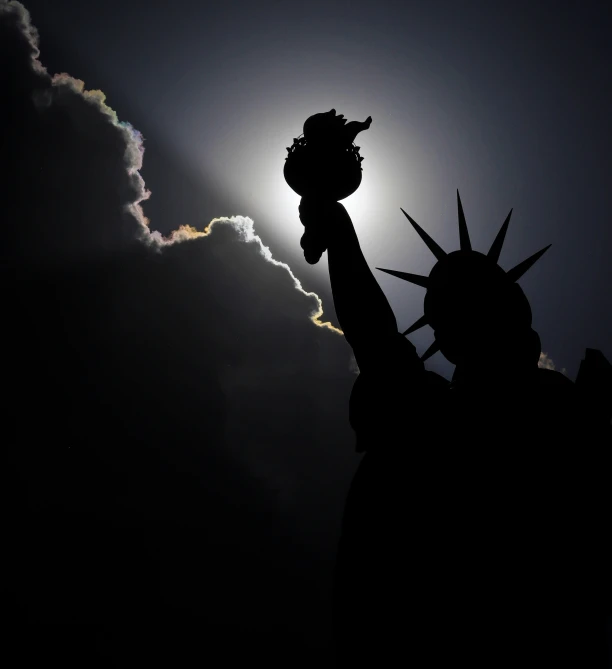 the statue of liberty is silhouetted against a cloudy sky