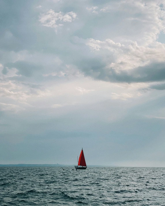 a lone boat in the middle of a body of water under a cloudy sky