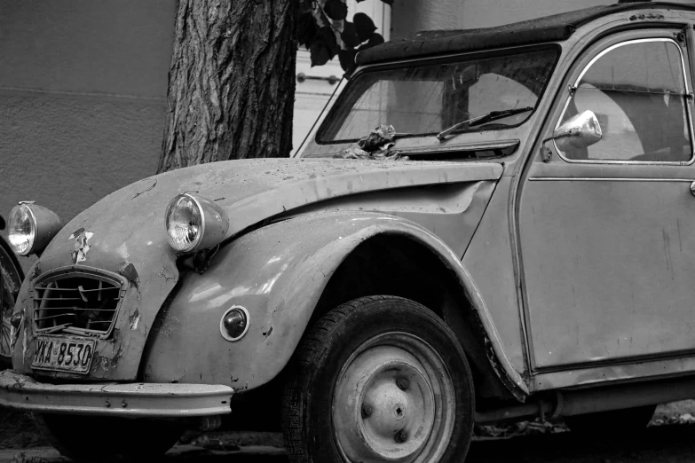 a very old, run down looking car parked next to a tree