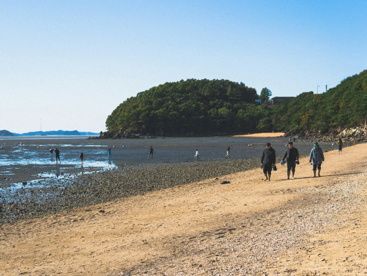 some people walking across a beach by water