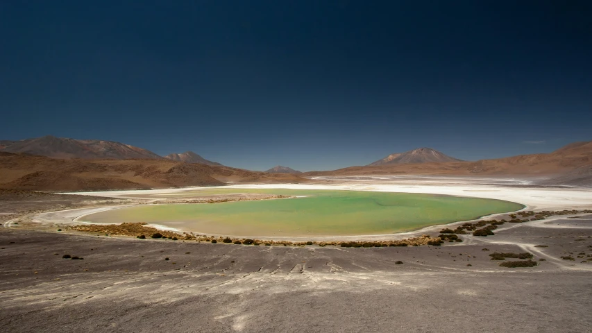 a barren landscape with an artificial green lake in the center