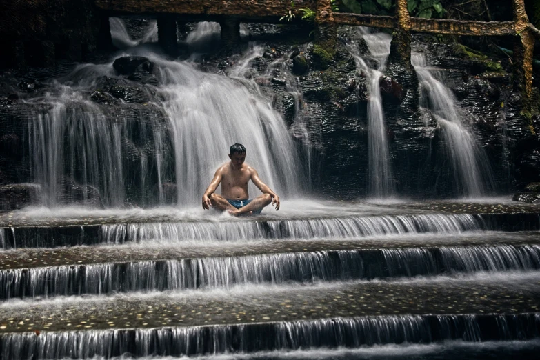 the man is sitting on steps in front of a waterfall