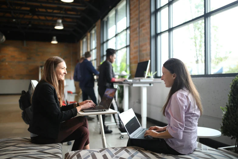 two women are sitting on the floor with laptops