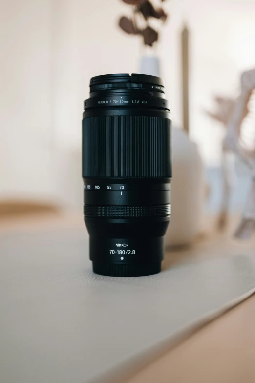 a camera lens sits on a table beside a flower vase