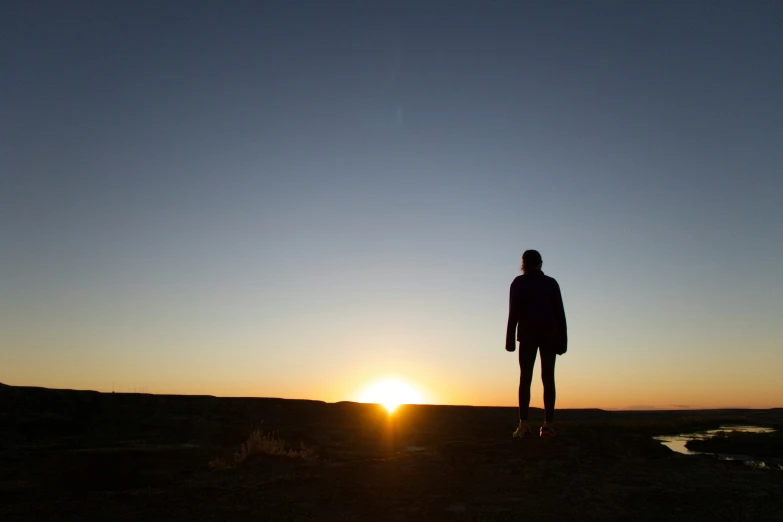 the silhouette of a woman at sunset overlooking a body of water