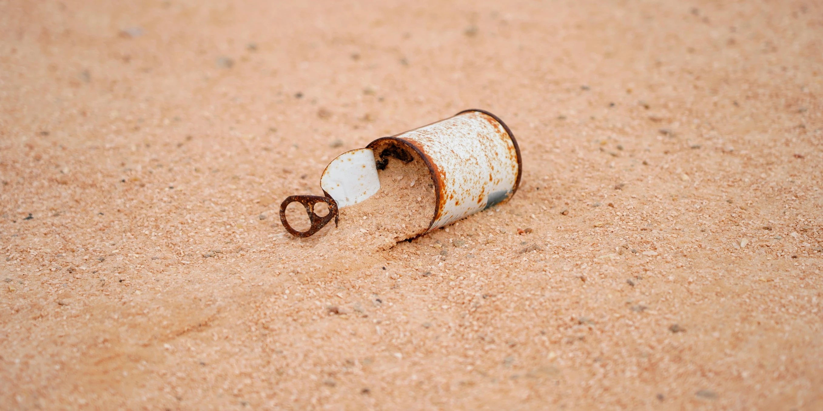 a white can with brown scissors attached lies on a sandy ground