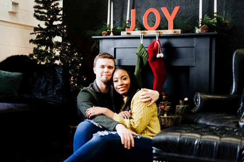 two people sit on a couch near a fireplace with a merry stocking