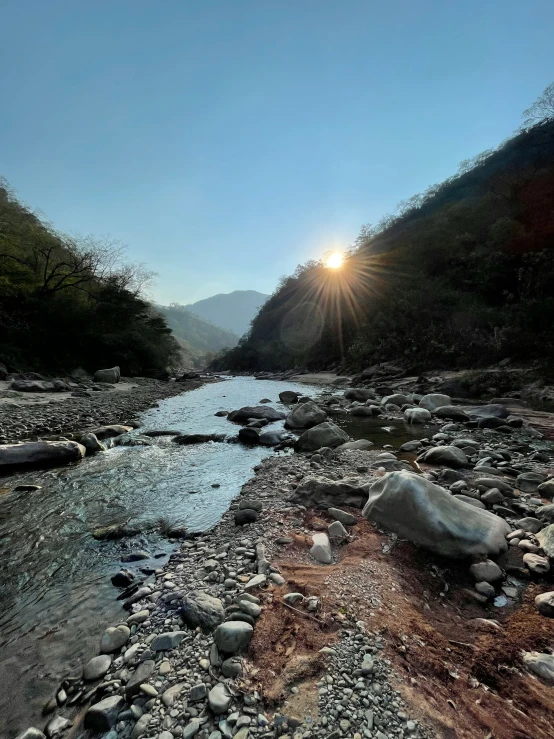 the sun is seen rising over a mountain river