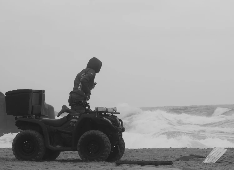 two people stand on four wheelers with a boat in the background