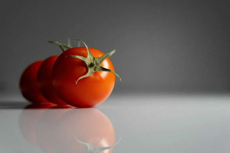 two tomatoes are on the table reflecting it's own image