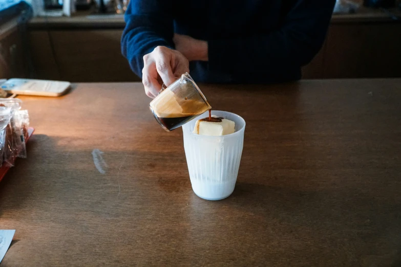 someone putting soing into a cup and another is sitting at the table