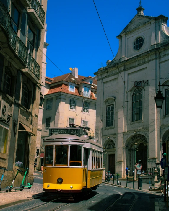 a yellow tram travels through an alleyway with old buildings