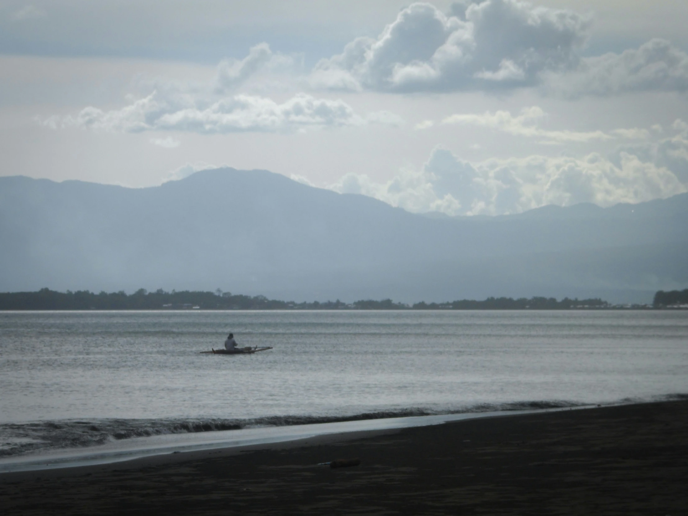 someone in a boat on the water with mountains in the distance