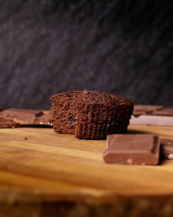 a chocolate muffin on a wood counter surrounded by chopped chocolate chunks