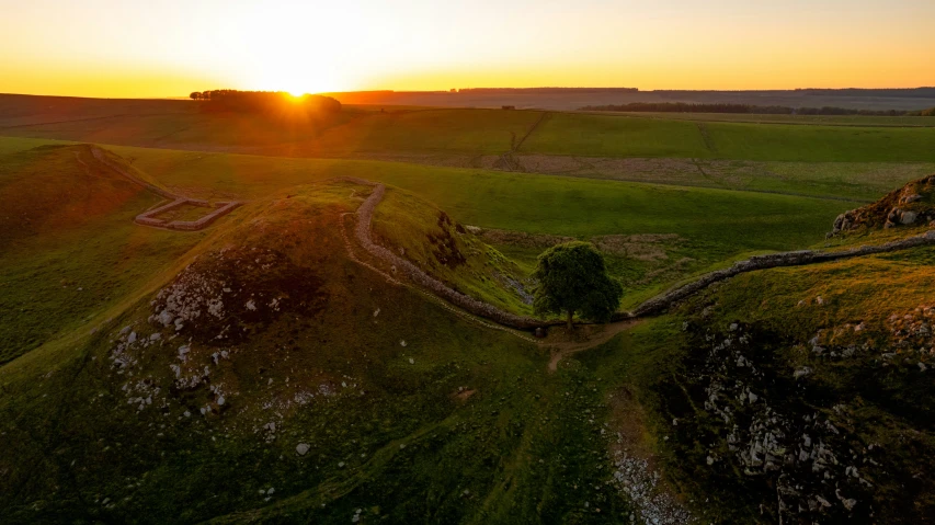 the sun is setting over the hills near a field