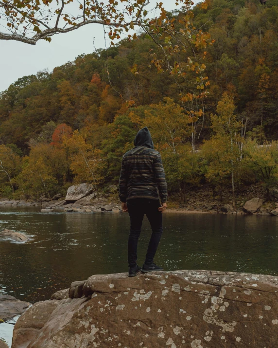 a man stands at the edge of a lake on an overcast day