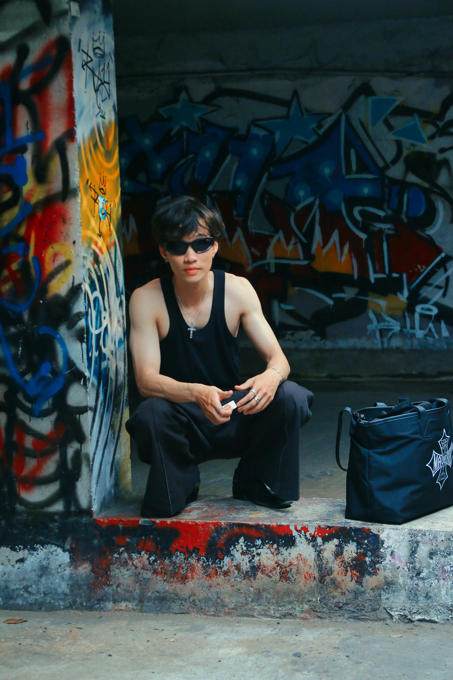 a man with a camera sitting by a graffiti covered wall