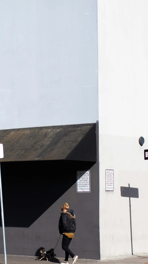 a woman walking her dog in front of a gray wall