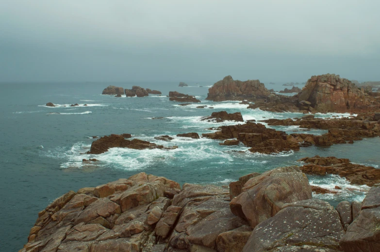 a rock covered ocean filled with waves next to a sandy shore