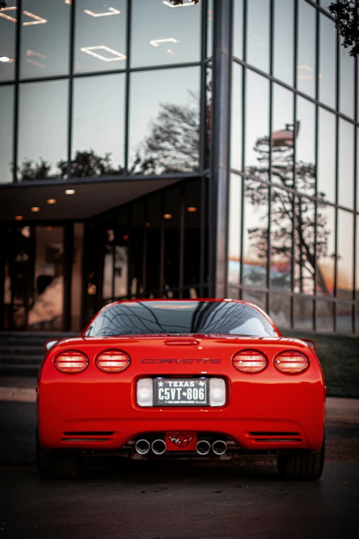 a bright red sports car sits parked outside of an office building