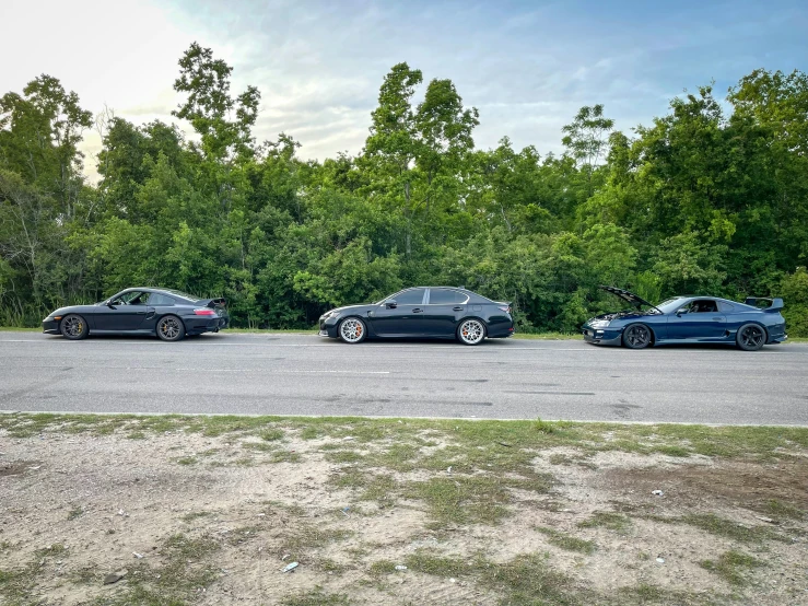 three modern cars parked on a parking lot surrounded by trees