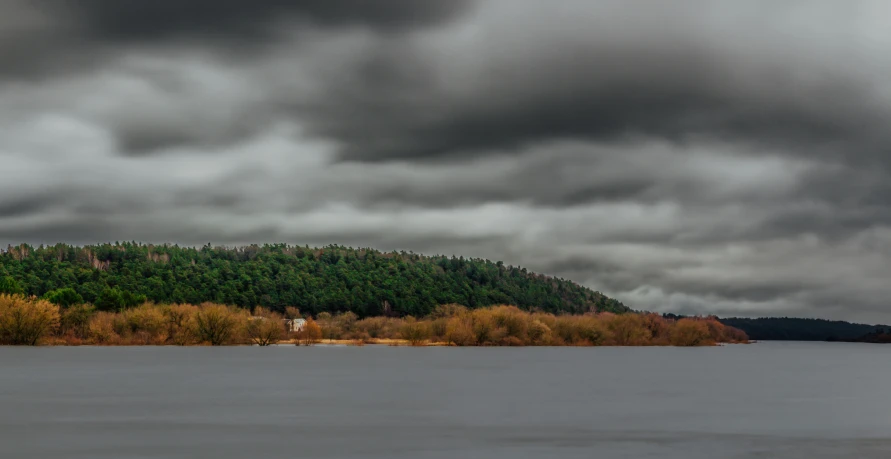 a lake sitting under a cloudy sky with trees lining the shore