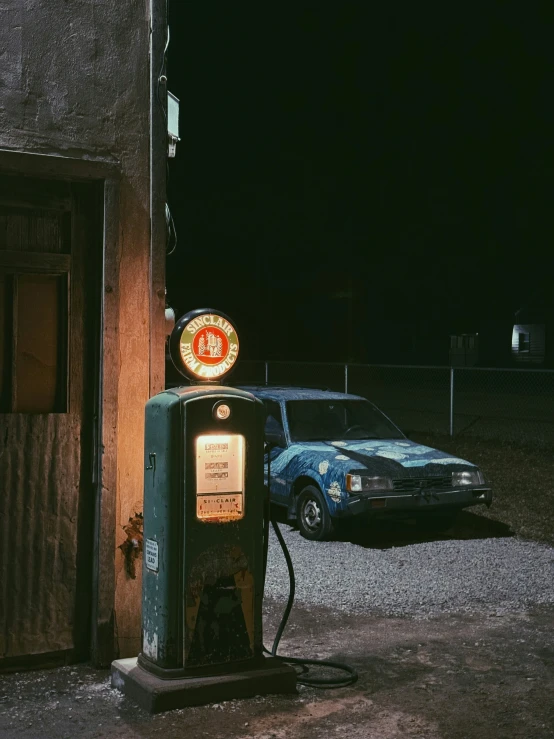 an old green gas pump sitting next to a blue car