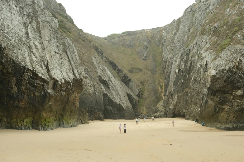 two people walking in the sand near a large cliff