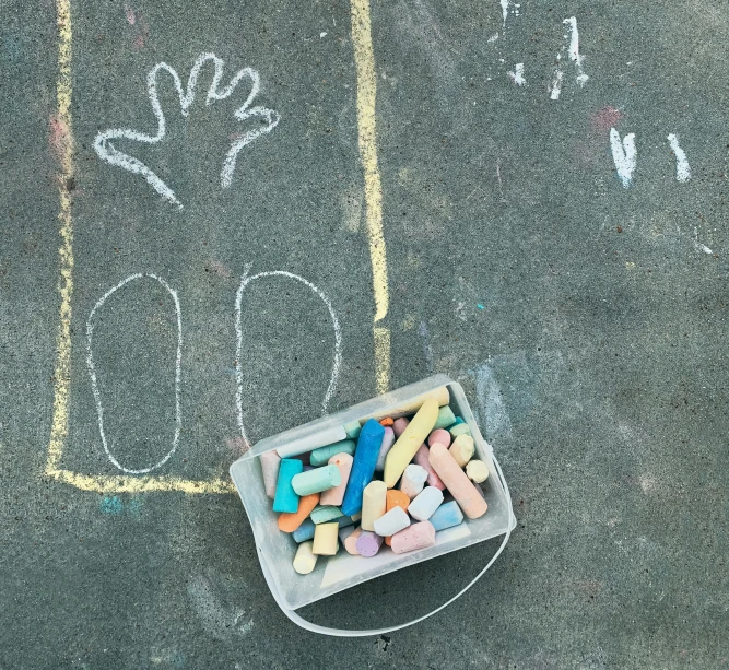 chalk writing on the sidewalk next to a bucket full of crayons