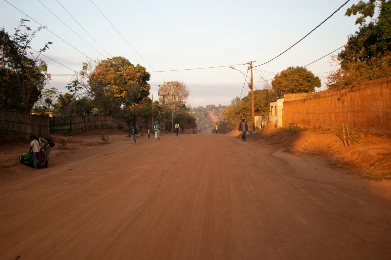 a dirt road leading to several houses with a few people walking down the road