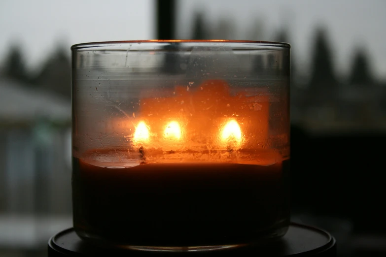 four lit candles glowing orange inside of a clear glass vase