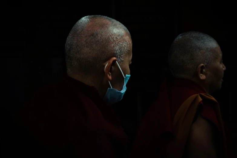 two monks are in the dark, one wearing a surgical mask