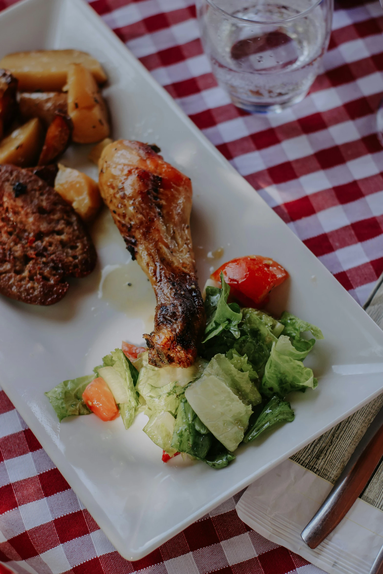 a plate with some chicken, potatoes and salad on a table cloth