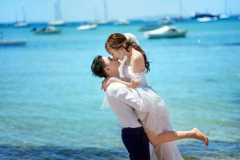 two women in white outfits are kissing on the beach