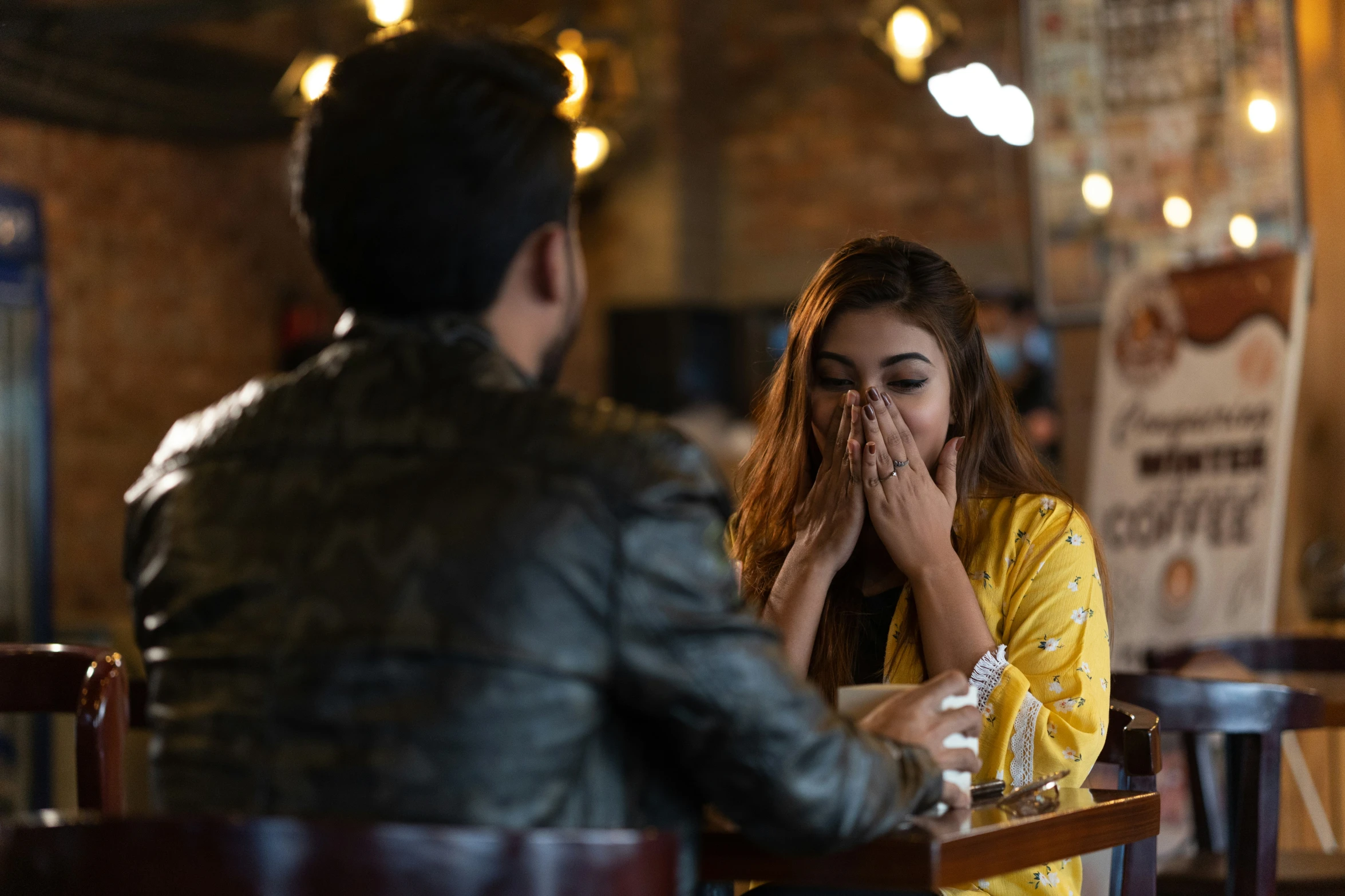 two people sitting at a table in a restaurant with their hands to their mouth