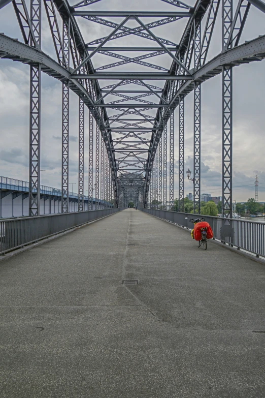 person with red umbrella kneeling by large bridge