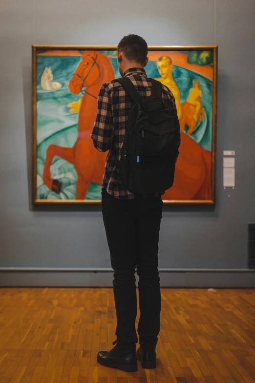 a man in a checkered shirt stands in front of paintings